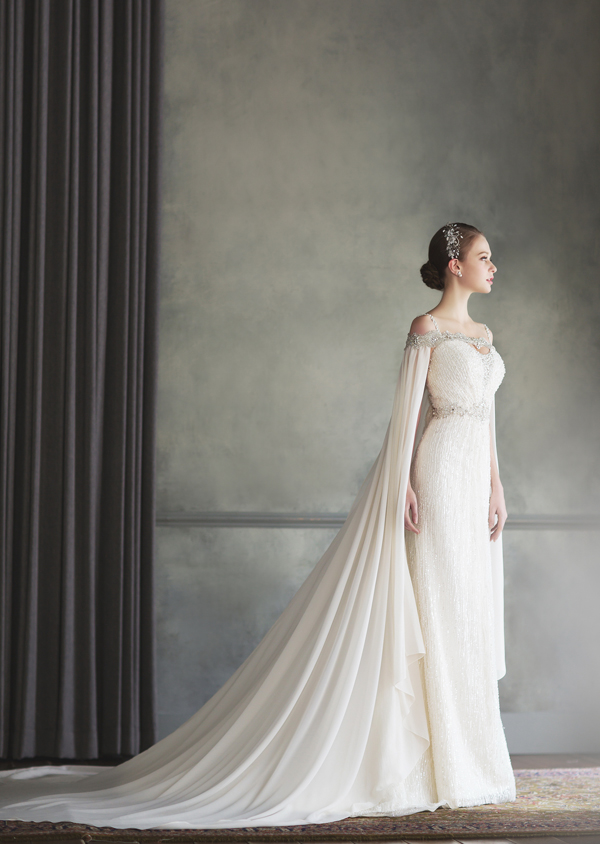 How beautiful is this Bonheur Sposa gown featuring an unique off-the-shoulder jeweled neckline and a stylish cape!